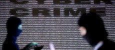 People wearing balaclavas are silhouetted as they pose with a laptops in front of a screen projected with the word cyber crime.