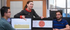 Professor Dina Katabi (center) explains how PhD student Fadel Adib's (right) face is neutral but that EQ-Radio's analysis of his heartbeat and breathing show that he is sad.