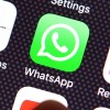 A user's finget is seen over a WhatsApp logo on a smartphone screen.