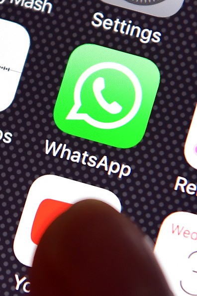 A user's finget is seen over a WhatsApp logo on a smartphone screen.