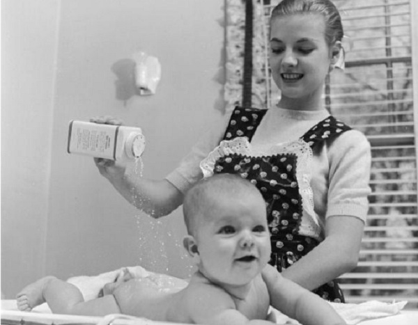 A young mother pours talcum powder over her baby daughter. 