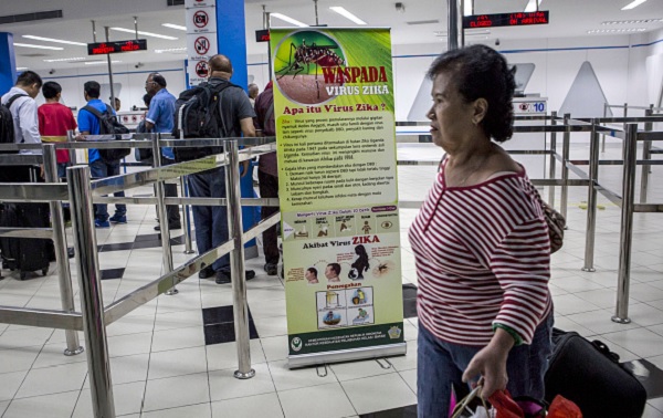  Ferry passengers arriving from Singapore walk near a banner about the Zika virus .